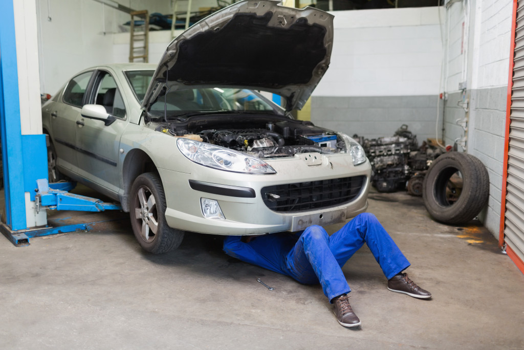 A car mechanic working in a garage, fixing the underside of a car