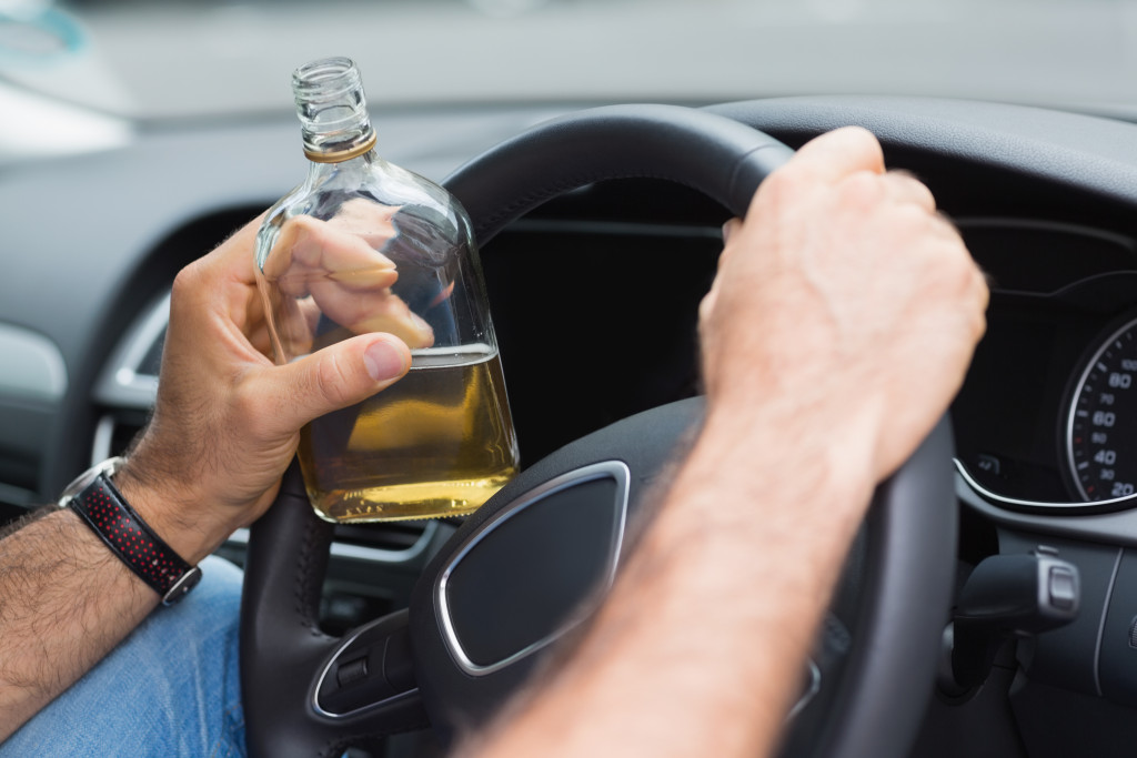 Person holding a bottle of alcoholic beverage while driving.